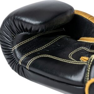 Corbetti CTG-001 Black-Gold Muay Thai Glove laying down on its fist side palm up showcasing the kevlar thread stitching