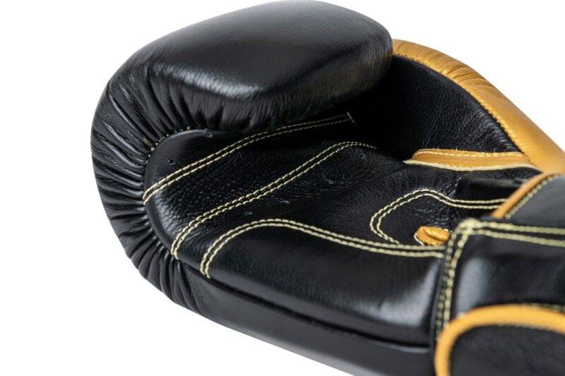 Corbetti CTG-001 Black-Gold Muay Thai Glove laying down on its fist side palm up showcasing the kevlar thread stitching